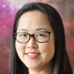 A woman with long dark hair and glasses smiles in front of a colorful, blurred background that resembles a nebula or galaxy, suggesting the inspiring atmosphere of creative webinars.