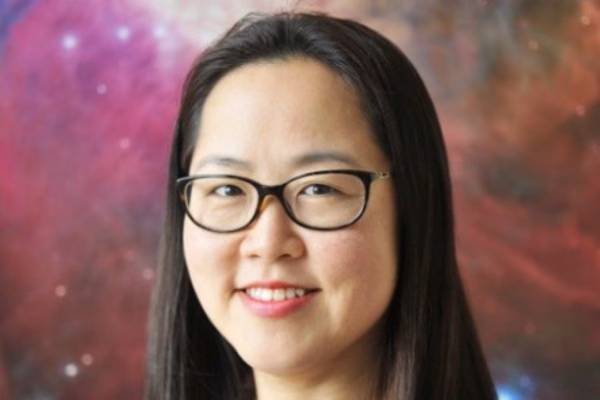 A woman with long dark hair and glasses smiles in front of a colorful, blurred background that resembles a nebula or galaxy, suggesting the inspiring atmosphere of creative webinars.