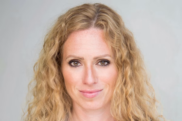 A woman with long curly blonde hair and light eyes looks forward, smiling slightly, against a plain light background—ready to inspire confidence in her next series of webinars.