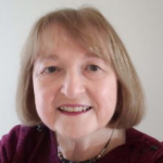 Dr. Ellie Cantor smiles at the camera wearing a maroon shirt, lipstick and a light brown bobbed haircut
