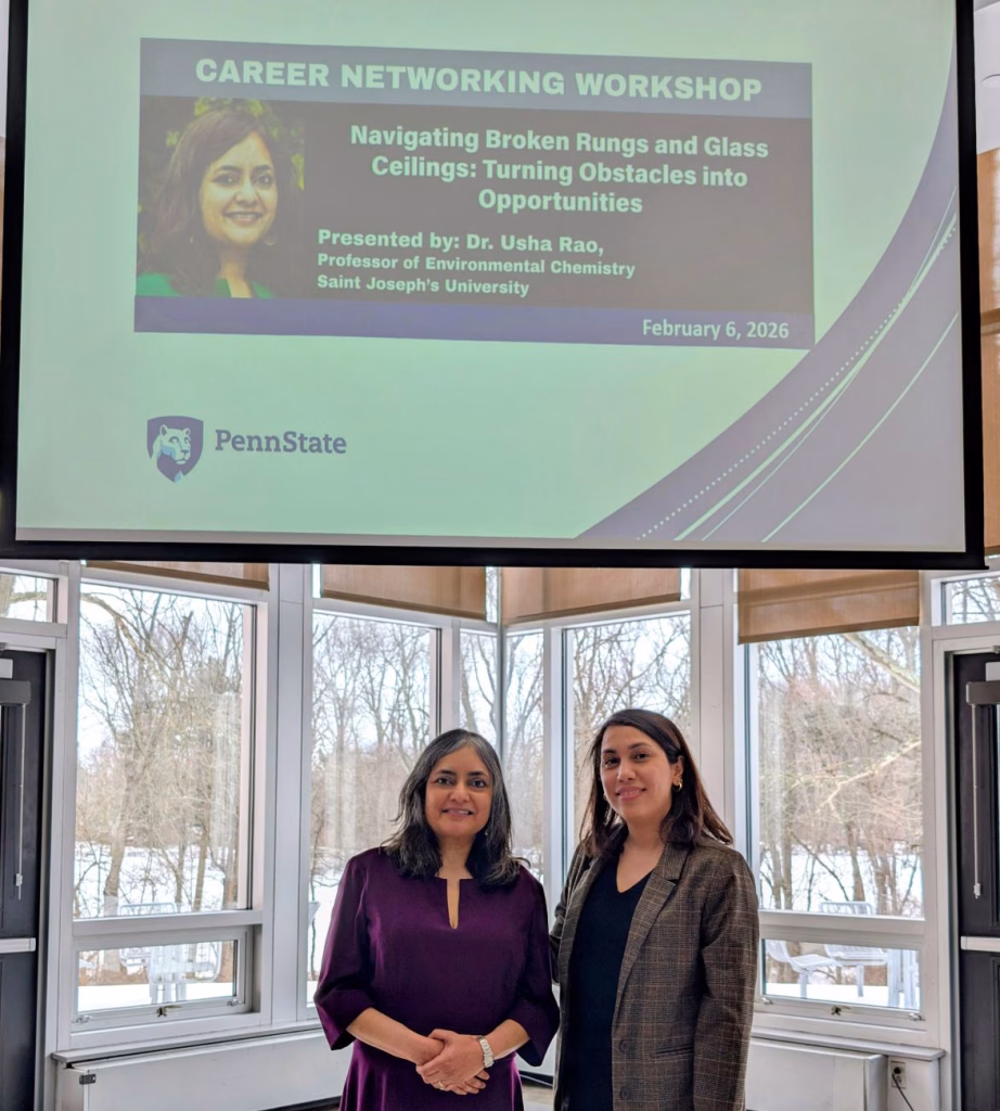 Two women stand indoors under a large projected slide for a Career Networking Workshop by Dr. Usha Rao at Penn State, with windows showing snowy trees in the background.