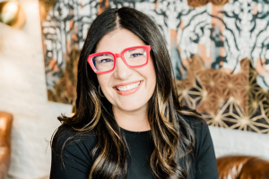 AWIS speaker, Rebecca Malotke-Meslin, smiles, and wears a black shirt with red glasses.