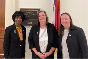 Three women stand smiling in front of an office door with a sign reading Representative Valerie P. Foushee, North Carolina and the number 2452. A U.S. flag is visible in the background.