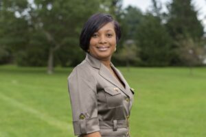 Headshot of Elise Lewis, an African American woman with a bob haircut, with green grass and trees in the background.