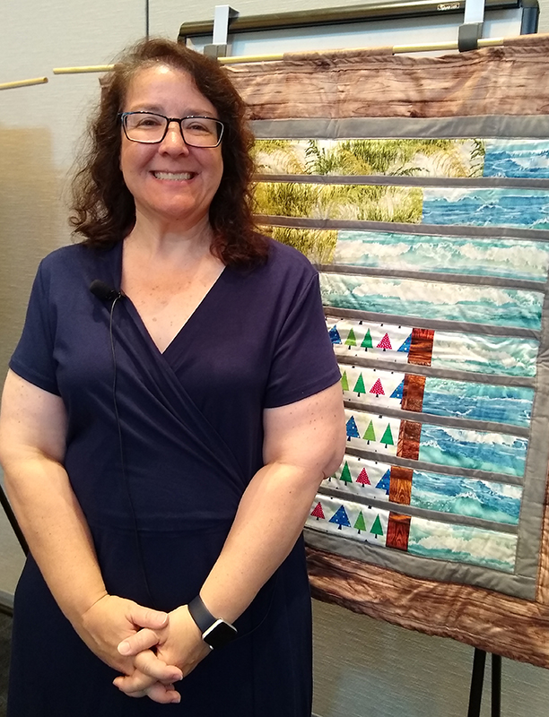 Laura Guertin standing by her first-ever science-themed quilt, from the Stitching Hope for the Louisiana Coast collection.