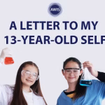 Two girls wearing safety goggles and lab coats hold up flasks with colored liquids (one red, one blue), smiling. Text above them reads, “A Letter to My 13-Year-Old Self.” AWIS logo is at the top.