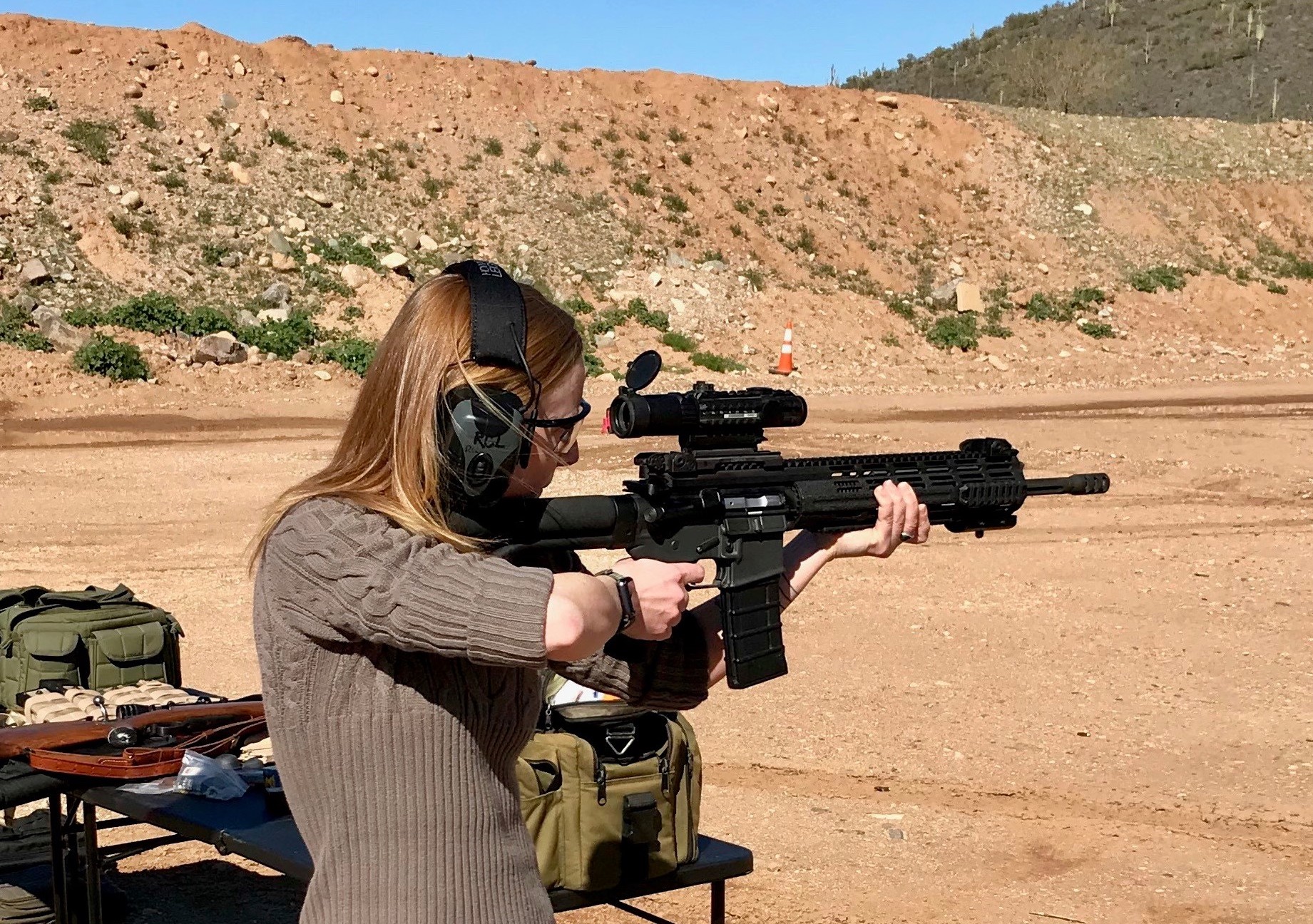 Rebecca at an outdoor shooting range test firing a rifle, one aspect of her job duties.