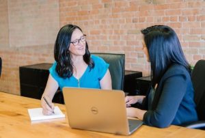 Two women sitting at a desk with a laptop open in front of them