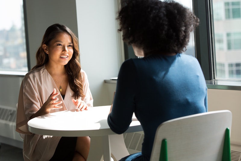 Two women sit across from each other at a table in an office setting.