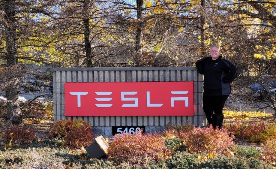 Corinne stands next to the Tesla sign.