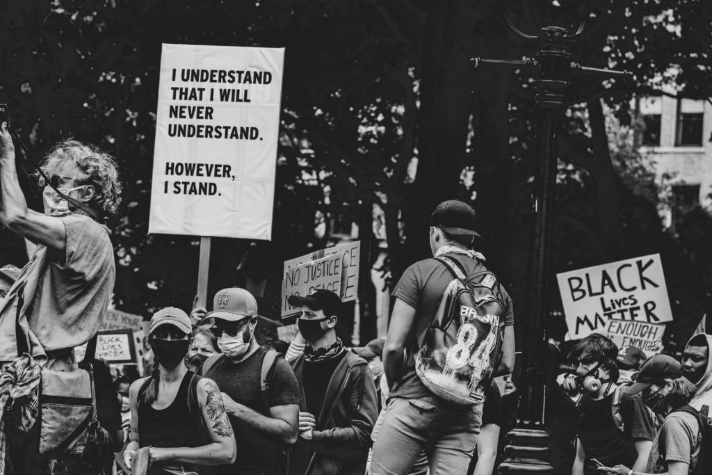 Photo of protesters one holding a sign that says "I understand that I will never understand. However, I stand."