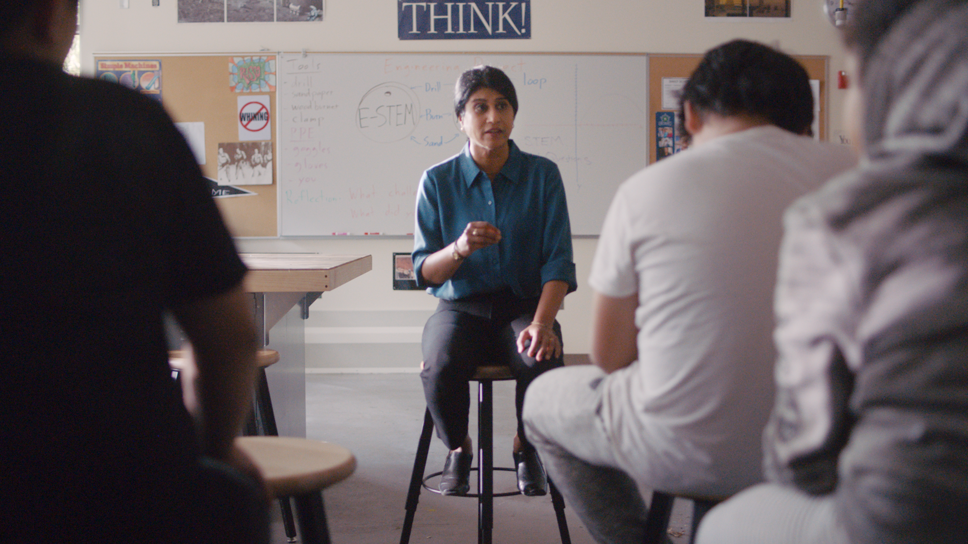 Dr. Seth sitting on a stool at the front of a science classroom talking to students