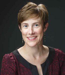 Headshot of Moriah Beck, who has short light hair and is wearing a red and black top. There's a black background.