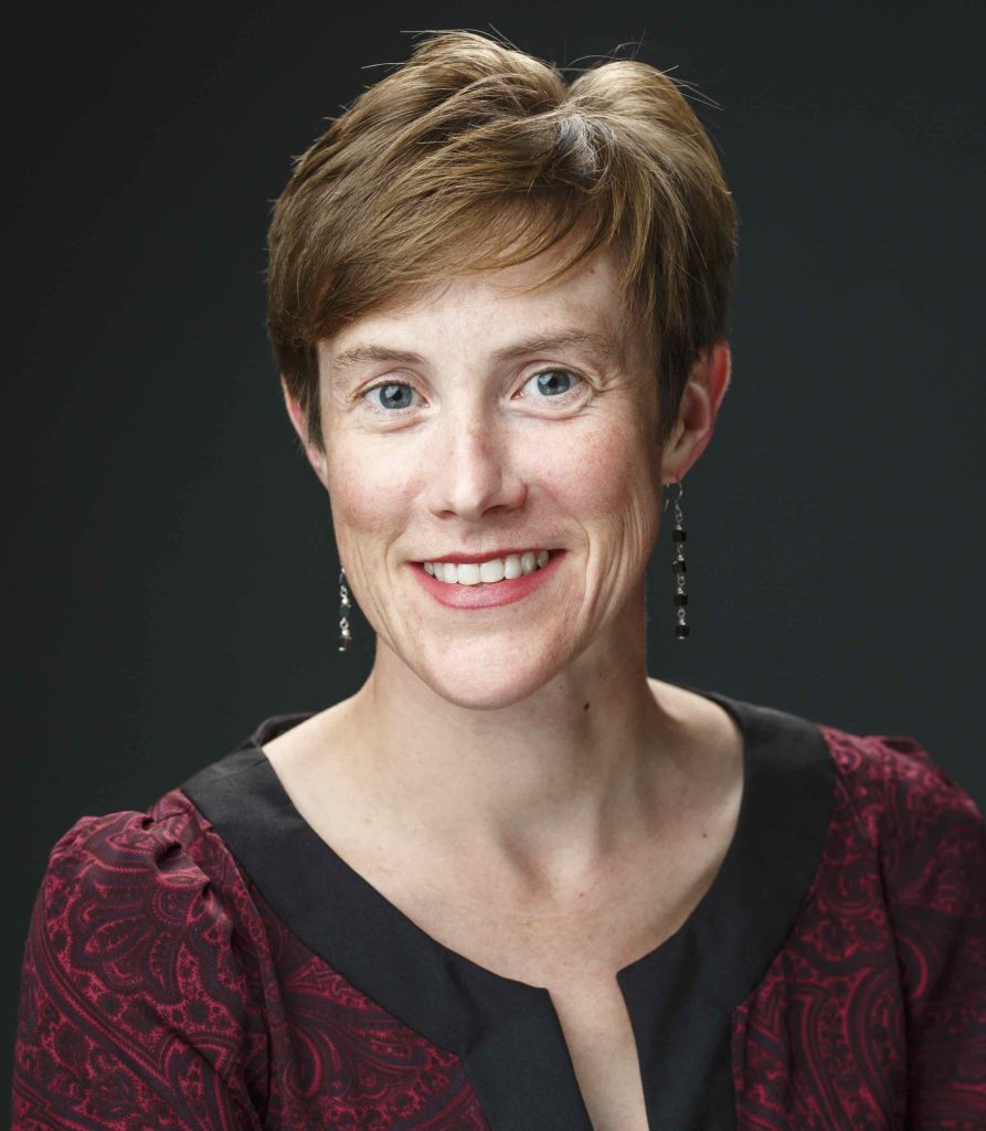 Headshot of Moriah Beck, who has short light hair and is wearing a red and black top. There's a black background.