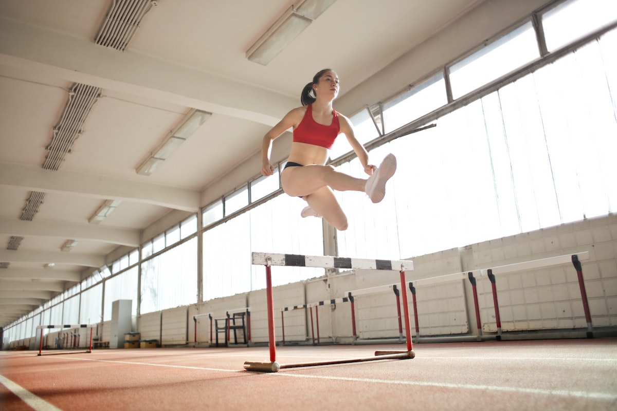 A lone woman jumps over a hurdle on an indoor track