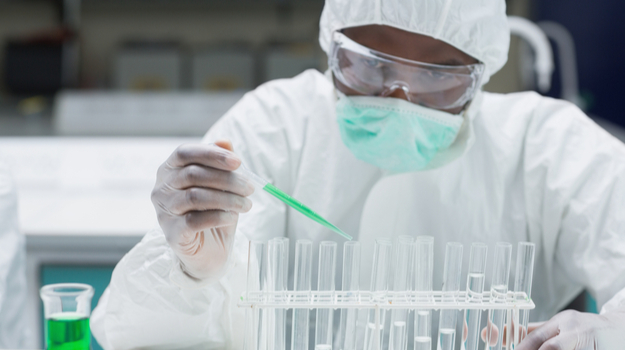 Chemist in protective suit filling test tubes with green liquid in the lab. Photo credit: Biospace.